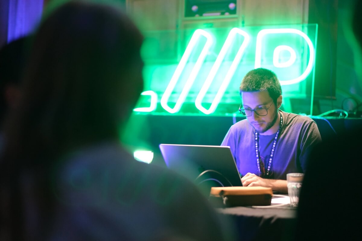David typing on his laptop in a dark environment and with a Liip neon sign in the background.